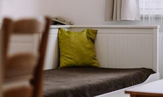 A cozy bedroom with a white bed and a green pillow. Next to the bed, there is a wooden table with a chair.