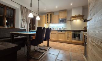 A modern kitchen with wooden cabinets and a dining area. The space is well lit and cozy furnished.