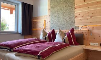 A cozy bedroom with a wooden bed and red pillows. Large windows let in plenty of light and create an inviting atmosphere.