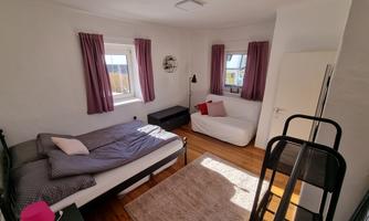 A simple bedroom with a single bed and a sofa bed. The room has light walls and curtains in purple.