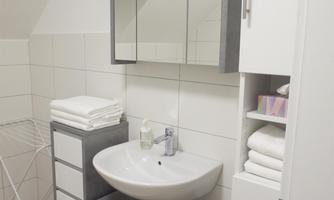 A modern bathroom with a sink, a mirror, and storage space. White tiles and soft towels create a bright, inviting atmosphere.