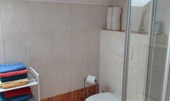 A bathroom with a toilet and a shower.  
Colorful towels are stacked on a rack.
