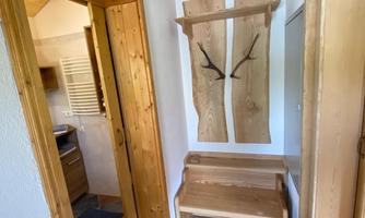 A friendly entrance area with wooden details and a bench. The walls are light, and a small kitchen is visible.