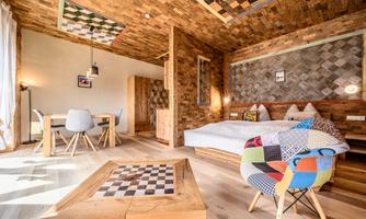 A modern room with wooden walls and a cozy bed. There is a dining table and a colorful armchair that gives the room a vibrant character.