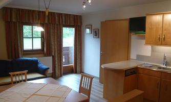 A bright and inviting apartment with an open kitchen and a cozy living room. The dining area is equipped with a table and chairs and has large windows for ample daylight.