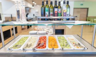 A buffet with various fresh ingredients like vegetables and salad. Above are bottles with different oils for seasoning.