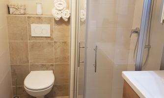 A modern bathroom with a shower, a toilet, and a washbasin. The walls are brightly tiled and there are fresh towels.