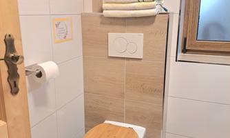 A modern bathroom with a wooden toilet and fresh towels. The walls are brightly tiled, and a window lets in natural light.