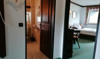 A view into a room with an open bathroom. There is a table and chairs as well as a bed in the background.