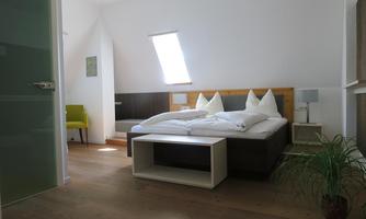 A cozy room with a double bed and white bedding. There is a green seating area and plenty of daylight through the window.