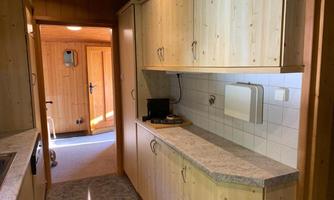 A bright kitchen with wooden cabinets and a green countertop. In the background, an entry to another room is visible.