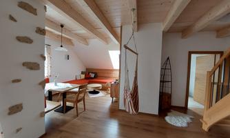 A modern living room with wooden ceilings and a cozy dining area. On the right side, there is a staircase that leads to additional rooms.