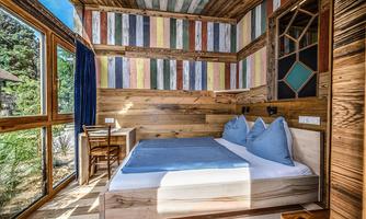 A cozy bedroom with wooden furniture and colorful walls. Large windows provide plenty of light and a beautiful view of nature.