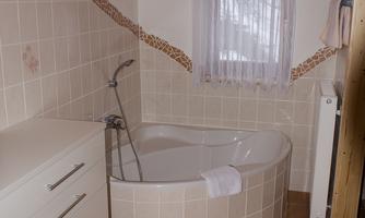 A modern bathroom with a round bathtub and bright tiles. The wooden ceiling and the windows give the room a cozy atmosphere.