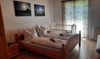 A cozy bedroom with two beds and a baby crib. Bright walls and windows with curtains create an inviting atmosphere.