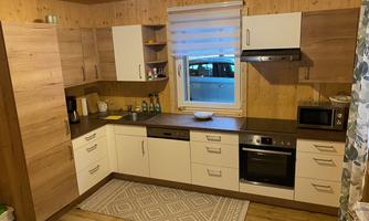 A modern kitchen with wooden furniture and a clear layout. It features basic kitchen appliances and windows with natural light.