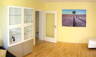 A bright room with yellow walls and a wooden floor. A glass display case is on the left, while a large picture of a lavender field landscape hangs on the wall.