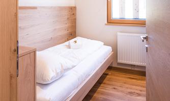 A simple bedroom with wooden floor and a single bed. The room has a window that lets in light.