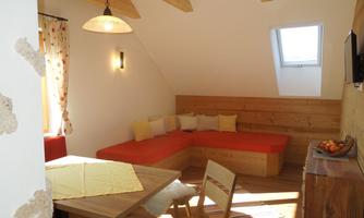 A cozy living space with an orange seating area and a wooden table. Large windows provide plenty of daylight and a friendly atmosphere.