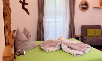 A cozy bedroom with a large bed and soft pillows. The room has bright wood and a large window front that lets in daylight.