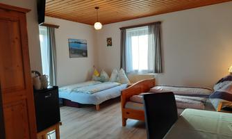 A cozy bedroom with two single beds and a double bed. There is wooden paneling on the ceiling and windows with plenty of natural light.