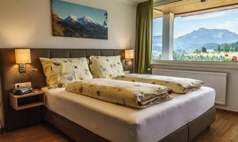 A cozy hotel room with a double bed and a view of the mountains. Large windows let in plenty of daylight.