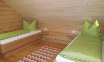 A cozy bedroom with two single beds and green cushions. The room features a wood design and a colorful carpet.