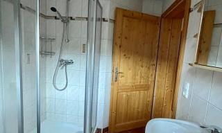 A small bathroom with a shower and a sink. The walls are tiled and the door is made of wood.