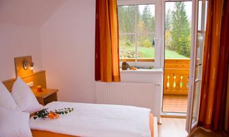 A cozy room with two beds and warm colors. The view of the balcony and the green landscape creates an inviting atmosphere.