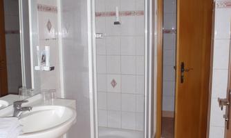 A modern bathroom with a shower cabin and a sink. The walls are tiled in light colors and a wood stove is visible.