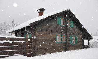 A cozy wooden house in the snow, surrounded by winter landscape. Large snowflakes are falling and the windows are painted green.
