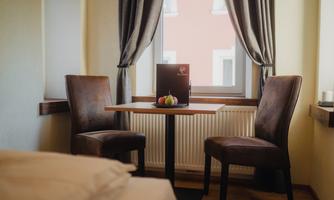A cozy table with two chairs is placed by a window decorated with curtains. On the table, there is a menu and some fruits.