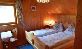A cozy wooden bedroom with two beds and a warm atmosphere. A table and a chair complement the space.