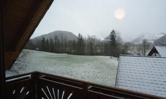 A snowy landscape with mountains in the background. On the balcony, a rustic wood design can be seen.