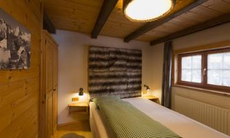 A cozy bedroom with wooden walls and a large window. The two beds are equipped with checked bed covers and a decorative wall paneling.