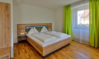 A modern bedroom with a double bed and wooden furniture. Large windows let in plenty of light, and the green curtains add a fresh touch.