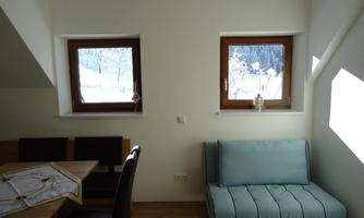 A cozy room with a blue sofa and a dining table. Outside, you can see snow-covered trees through the windows.