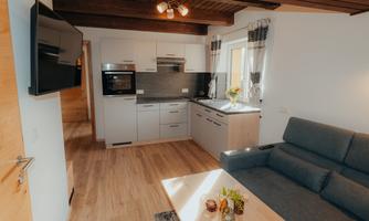 A modern kitchen with a cozy living area. There is a gray sofa and light wood details.