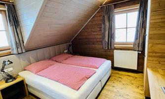 A cozy bedroom with a double bed and wooden paneling. There are two windows that let natural light in.