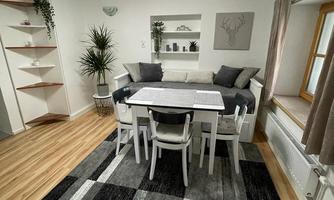 A cozy dining area with a table and white chairs. The room has a modern style with wooden flooring and decorative elements.
