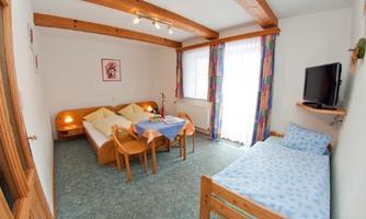 A cozy room with two beds and a single bed.  
There is a table and a television, as well as large windows with colored curtains.