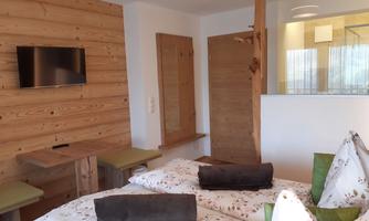A modern room with wood paneling and two beds. A television hangs on the wall and there is a bright, friendly atmosphere.
