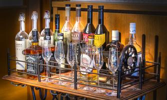 A bar with various bottles of alcoholic beverages and glasses. The bottles are placed on a wooden rack and are well-lit.