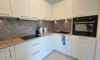 A modern kitchen with white cabinets and an elegant gray countertop. It is equipped with a stove, an oven, and modern kitchen appliances.