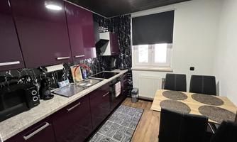 A modern kitchen with purple cabinets and a dining table. The decor is stylish and functional.