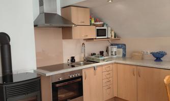 A modern kitchen with wooden furniture and modern appliances. The floor is made of wood and there is a fireplace in the corner.