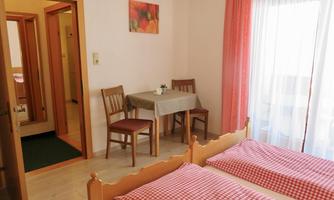 A cozy room with two beds and checkered cushions. There is a small table with chairs and plenty of daylight coming through the window.