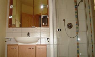 A modern bathroom with a sink, mirror, and a shower. The walls are tiled, and there are wooden details.