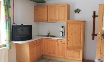 A simple kitchen with wooden cabinets and a small washing area. There is a television and a kettle on the countertop.