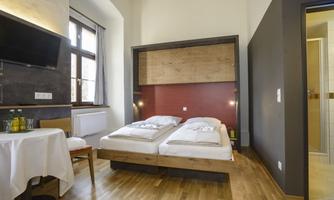 A modern room with two single beds and wooden flooring. Featured are a table, a television, and an adjacent bathroom.